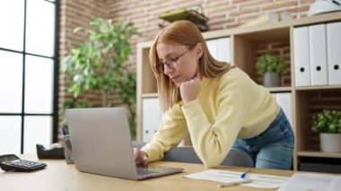 Ofiste çalışan genç sarışın iş kadını dizüstü bilgisayar kullanıyor.