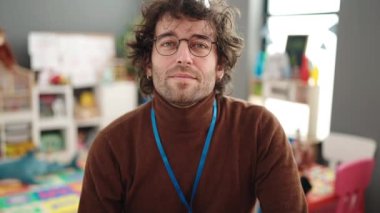 Young hispanic man preschool teacher smiling confident doing ok gesture at kindergarten