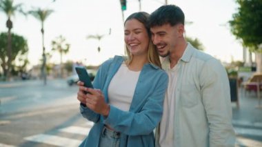 Young couple smiling confident using smartphone at street