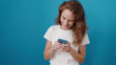 Genç, güzel İspanyol kadın, kendine güvenen, mavi arka plan üzerinde akıllı telefon kullanan.