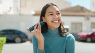 Genç Afrikalı Amerikalı kadın gülümsüyor. Caddedeki akıllı telefondan kendine güvenen sesli mesaj dinliyor.