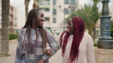 İki Afro-Amerikan kadını parkta kendinden emin bir şekilde gülümsüyor.