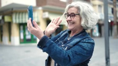 Middle age woman with grey hair smiling confident having video call at street