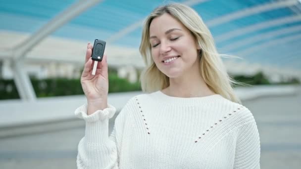 年轻的金发女子自信地微笑着 指着停车场的新车钥匙 — 图库视频影像