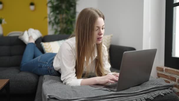 Young Blonde Woman Using Laptop Lying Sofa Home — стоковое видео