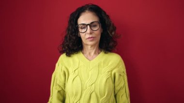 Middle age hispanic woman doing negative gesture with thumb down over isolated red background