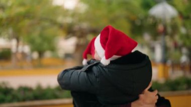 Anne ve oğul noel şapkası takıp parkta birbirlerine sarılıyorlar.