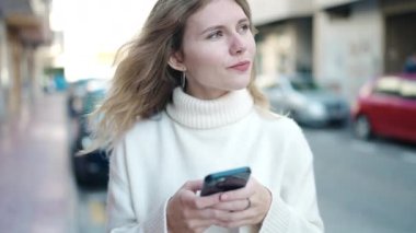 Sokakta akıllı telefon kullanan, kendine güvenen genç sarışın kadın.