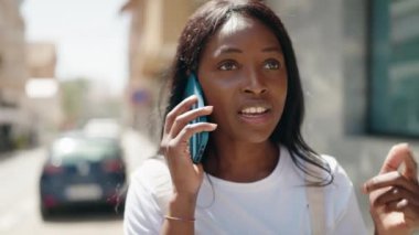 Genç Afrikalı Amerikalı kadın gülümsüyor. Kendine güveni tam. Sokakta akıllı telefondan konuşuyor.