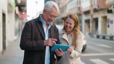 Orta yaşlı çift sokakta dokunmatik ped kullanarak gülümsüyor.