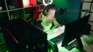 Young beautiful hispanic woman streamer playing video game using joystick at gaming room