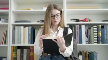 Young blonde woman student standing reading book at university classroom