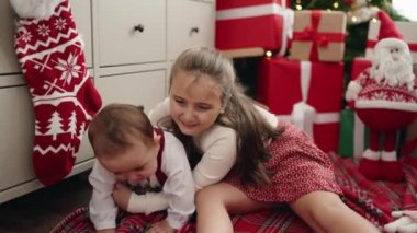 Erkek ve kız kardeşler Noel hediyeleriyle yerde oturup evde ağlıyorlar.