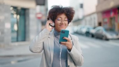 Afro-Amerikalı kadın gülerek sokakta müzik dinliyor.