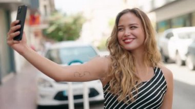 Genç ve güzel İspanyol kadın gülümsüyor. Kendine güveni tam. Sokakta akıllı telefonun yanında selfie çekiyor.