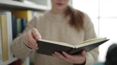 Young blonde woman student reading book doing silence gesture at library university