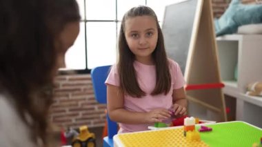 Adorable hispanic girl playing with construction blocks sitting on table at classroom