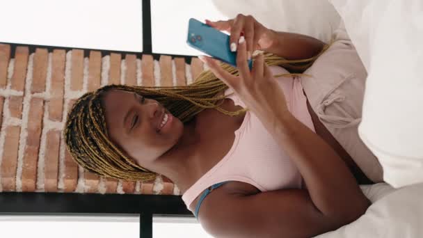 Afroamerikanerin Mit Smartphone Auf Bett Sitzend Vertikales Video Schlafzimmer — Stockvideo