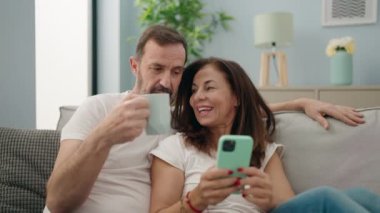 Man and woman couple drinking coffee using smartphone at home