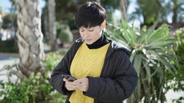 Young chinese woman smiling confident using smartphone at park