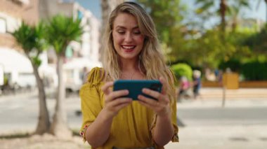 Young woman smiling confident watching video on smartphone at street