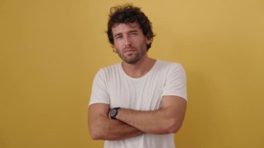 Kolları çapraz hareket eden genç İspanyol adam ve izole edilmiş sarı arka plan üzerinde ciddi bir ifade.