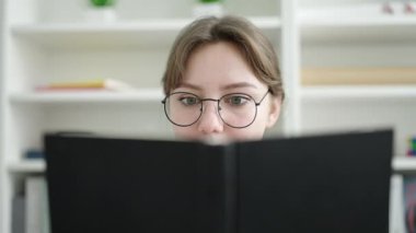 Young blonde woman student smiling confident reading book at library university