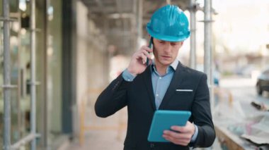 Young caucasian man architect using touchpad and talking on the smartphone at street