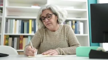 Orta yaşlı bir kadın, gri saçlı bir öğretmen, not defterine yazıyor. Üniversite sınıfında sırt ağrısı çekiyor.