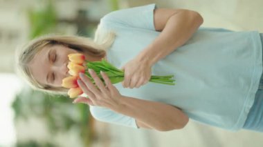 Young blonde woman smiling confident smelling flowers at street