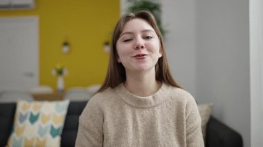 Young blonde woman having video call sitting on sofa at home