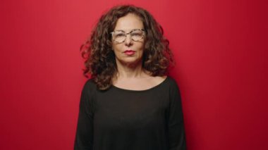 Orta yaşlı bir kadın gülümsüyor. Kollarını kavuşturup kırmızı arka plan üzerinde hareketler yapıyor.