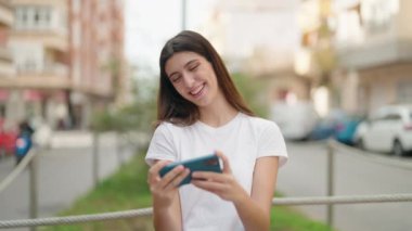 Genç İspanyol kız gülümsüyor. Sokakta akıllı telefondan videolar izliyor.