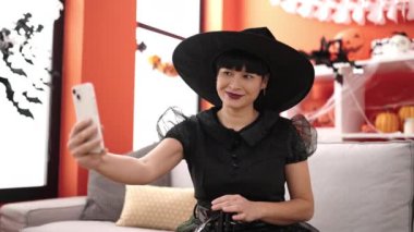 Cadı kostümü giyen genç Çinli kadın evde akıllı telefondan selfie çekiyor.