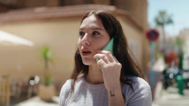 Gülümseyen genç bir kadın caddedeki akıllı telefondan konuşuyor.
