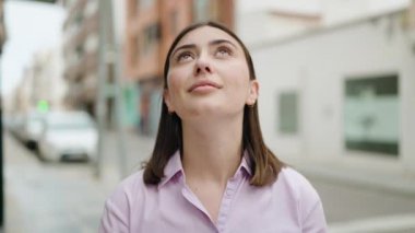 Young hispanic woman smiling confident looking to the sky at street