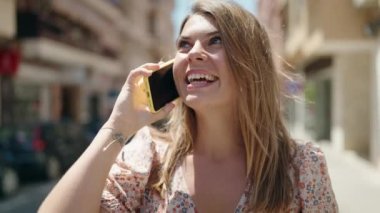 Gülümseyen genç bir kadın caddedeki akıllı telefondan konuşuyor.