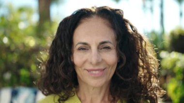 Orta yaşlı İspanyol kadın parkta kendinden emin gülümsüyor.