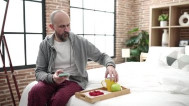 Genç kel adam kahvaltıya fotoğraf çekip yatak odasında oturuyor.