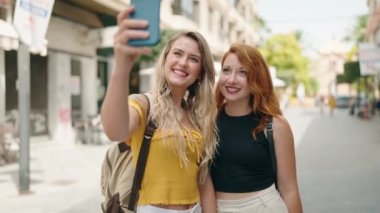 Two women standing together using smartphone at street