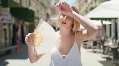 Young blonde woman using handfan at street
