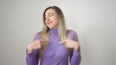 Genç sarışın kadın kendinden emin bir şekilde kendini işaret ederek izole edilmiş beyaz arka planda gülümsüyor.