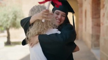 Two women mother and graduated daughter hugging each other at campus university