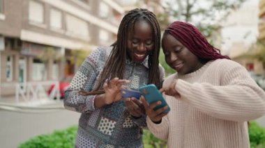 Two african american women using smartphone and credit card at street