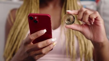 Afro-Amerikalı kadın akıllı telefon kullanıyor. Elinde bozuk para var.