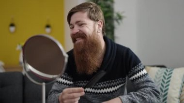 Evdeki kanepede oturan sakallı genç kızıl saçlı adam.