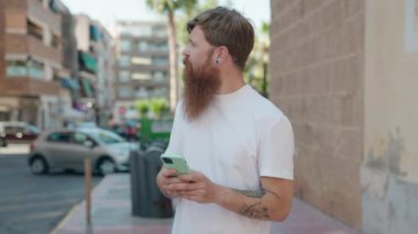 Young redhead man smiling confident using smartphone at street