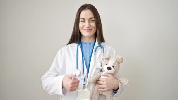 年轻的高加索女医生用大拇指托住孤立的白色背景的泰迪熊 — 图库视频影像