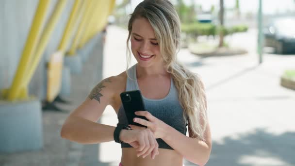Junge Blonde Frau Trägt Sportbekleidung Mit Smartphone Und Uhr Auf — Stockvideo