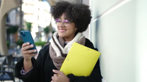 Joven Mujer Afroamericana Sonriendo Confiado Sosteniendo Carpeta Usando Teléfono Inteligente — Vídeos de Stock